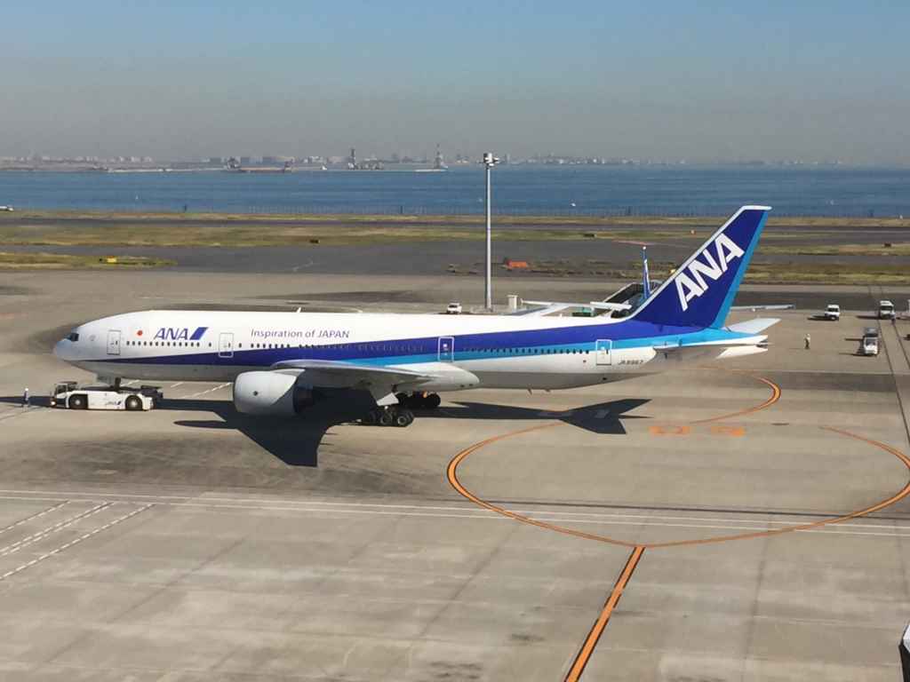 ANA 777 starting engines viewed from the obsdeck at Tokyo Haneda ANA Terminal 2 with Tokyo Bay in the background.