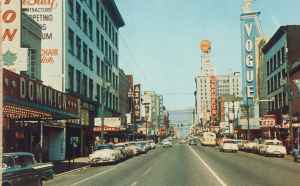 Granville Street Vogue and Orpheum Theatres circa 1954. Granville is Vancouver's busiest and most colourful street, showing the heart of the city's vibrant theatre district, with its numerous neon signs. (Grant-Mann Lithographers LTD "COLOR CARD" division, Vancouver, BC)